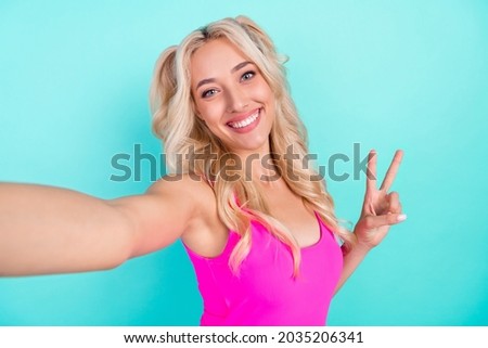 Self-portrait of attractive cheerful wavy-haired girl showing v-sign isolated over vivid teal turquoise color background