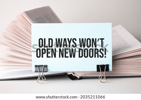 A white card with the text Old Ways won't open New Doors on a clip for papers on the table against the background of books. Defocus Royalty-Free Stock Photo #2035211066