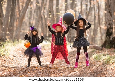 three little girls in witch costumes laugh, conjure, walk through the autumn forest with baskets for sweets in the shape of pumpkins. halloween concept, lifestyle . High quality photo
