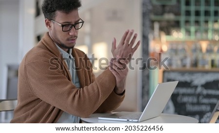 African Man having Wrist Pain while using Laptop in Cafe 