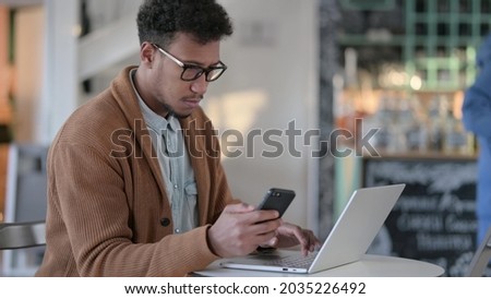 African Man with Laptop using Smartphone in Cafe