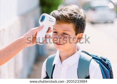 Teacher takes a child's temperature when entering school with an electronic thermometer. Covid-19 and virus pandemic concept Royalty-Free Stock Photo #2035233884