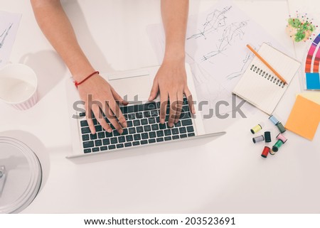 Hands of fashion designer working on laptop, view from the top