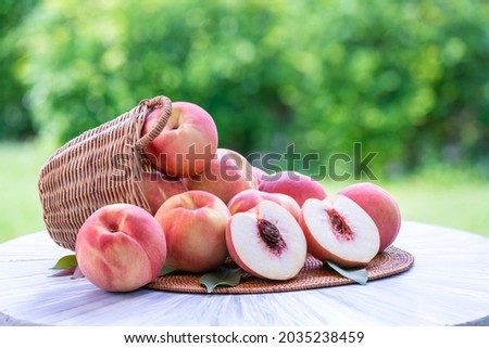 Fresh peach with slices on blurred greenery background, Peach fruit in Bamboo basket on wooden table in garden. Royalty-Free Stock Photo #2035238459