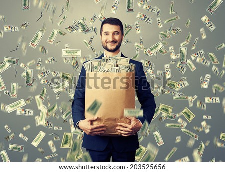 successful and smiley businessman holding paper bag with money under dollar's rain