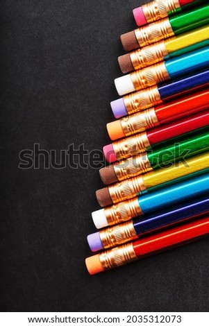 Colorful pencils with erasers in a row on a black background. Top view, free space