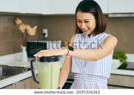 Pretty young Asian woman making smoothie in blender in the kitchen