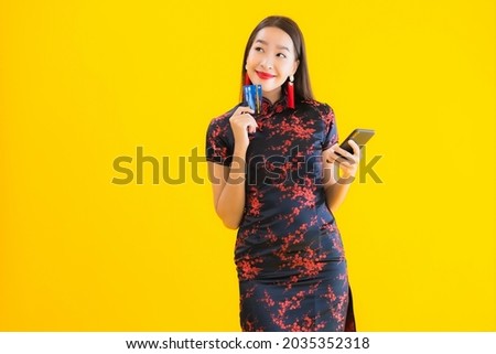 Portrait beautiful young asian woman wear chinese dress with credit card and smart mobile phone on yellow isolated background