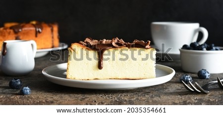 Cheesecake new york. Slice cheesecake with chocolate sauce and a cup of coffee on a dark concrete background.