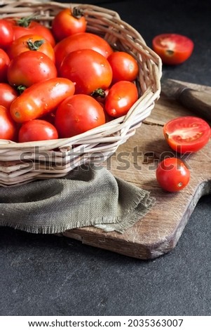 Fresh red tomatoes in whicker basket on black background.