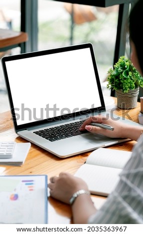 Cropped shot of woman hand working on laptop computer and peper work while sitting at the table, mockup blank screen for product display or graphic design.