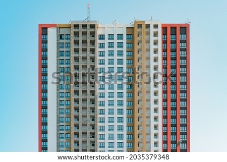 Red, white and black building under construction. Front view of apartment wall. Windows. Unfinished high-rise building. Finishing facade works. Wall insulation