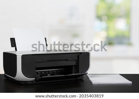 Compact laser printer on black desk against blurred background