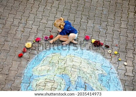 Little preschool girl with flowers and earth globe painting with colorful chalks on ground. Positive toddler child. Happy earth day concept. Creation of children for saving world, environment and