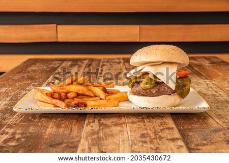 Beef burger with fried green peppers, tomato and onion slices and havarti cheese on top garnished with French fries