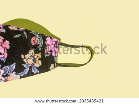 black and pink floral patterned cloth mask on a yellow background