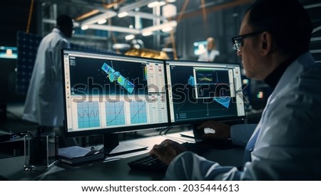 Male Engineer Uses Computer while Working on Satellite Construction. Aerospace Agency: Scientist is Using Computer Software for Programming and Assembly of Spacecraft for Space Exploration Mission. Royalty-Free Stock Photo #2035444613