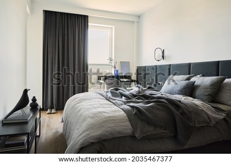 Stylish composition of small modern bedroom interior. Bed, creative lamp and elegant personal accessories. Walls with black panels. Panoramic windows. Minimalistic masculine concept. Template.

