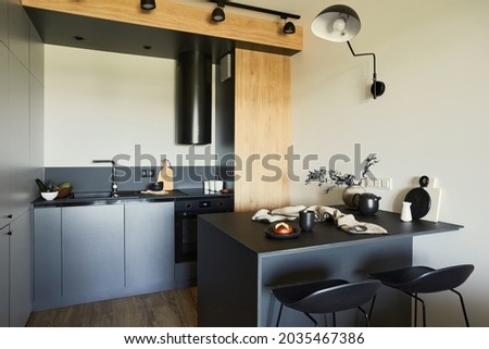 Stylish composition of modern small dining space interior. Black kitchen, kitchen island and dining accessories. Neutral walls. Minimalistic masculine concept. Details. Template.
