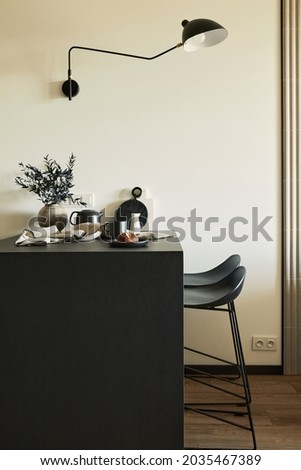 Stylish composition of modern small dining space interior. Black kitchen island and dining accessories. Neutral walls. Minimalistic masculine concept. Details. Template.
