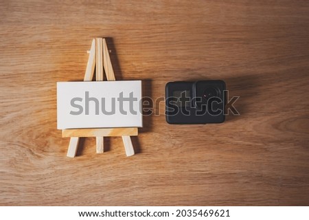 Mockup of a white business card on an easel with an action camera, on a wooden table background