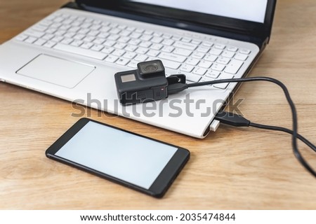 Mock up of a smartphone and an action camera connected to a white laptop on a wooden table background