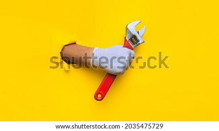 The doctor's hand in a white medical glove holds a red monkey wrench. Equal hole in yellow paper. The concept of retraining a doctor into a plumber, a specialist who does not do his own thing. Royalty-Free Stock Photo #2035475729