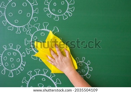 Coronavirus molecules drawn in white chalk on a green blackboard with white chalk and a human hand with a yellow rag erasing the drawing from the blackboard. Concept stop covid-19