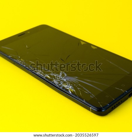 A mobile phone with a broken screen lies on a yellow background. A broken smartphone. Electronic gadget in need of repair.square image