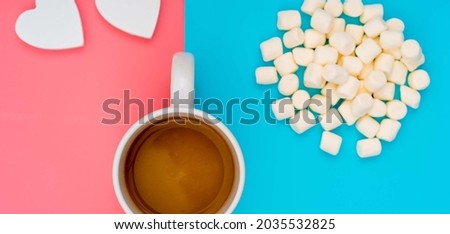 Cup of cocoa on a pink and turquoise background and marshmallows
