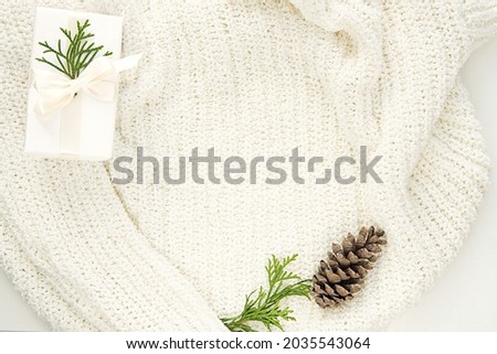 Winter, Christmas flat lay composition with warm white sweater, gift box and fir tree cone, space for text or design presentation.    