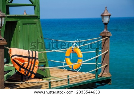 Rescue tower with lifebuoy and life jacket on a wooden pier. Sea background