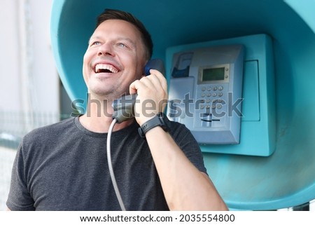 Smiling young man talking on phone booth on street Royalty-Free Stock Photo #2035554800