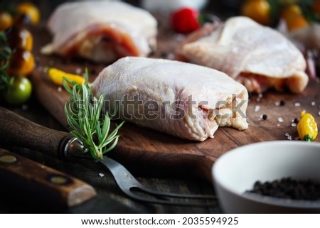 Raw uncooked chicken thigh meat over a wooden cutting board with fresh ingredients. Extreme selective focus with blurred foreground and background.
