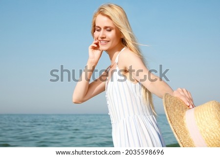 Beautiful young woman with straw hat near sea on sunny day in summer