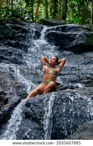 Young beautiful woman posing at small tropical waterfall