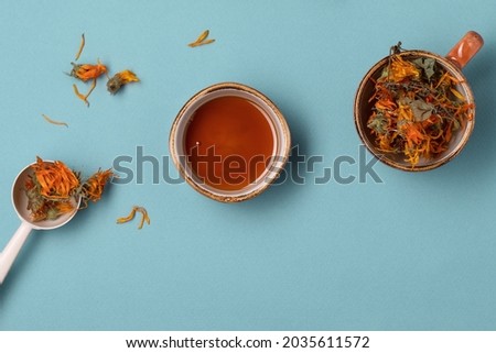 Calendula dried herbs in orange craft cup with honey on blue background