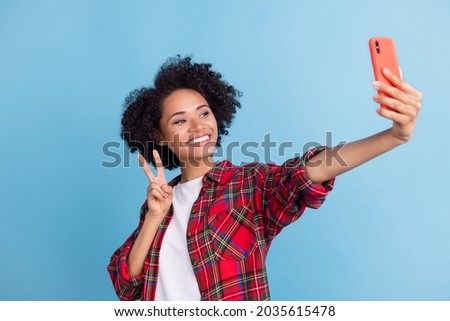 Photo of young afro girl happy positive smile make selfie smartphone show peace v-sign isolated over blue color background
