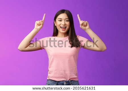 Charismatic good-looking lively smiling asian girl introduce product, pointing fingers up, indicate top advertisement, grinning toothy, excited telling good news, sharing link, purple background Royalty-Free Stock Photo #2035621631