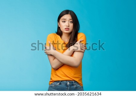 Girl feeling uncomfortable walking light yellow t-shirt, hugging herself trembling, shaking feeling cold, freezing windy weather, frowning grimacing discomfort, stand blue background Royalty-Free Stock Photo #2035621634