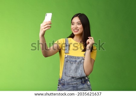 Glamour tender teenage asian female taking selfie, checking haircut, look smartphone front camera, photographing, record video message post online, smiling lovely, green background