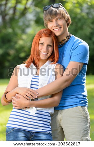Romantic teenage couple hugging in sunny park smiling at camera