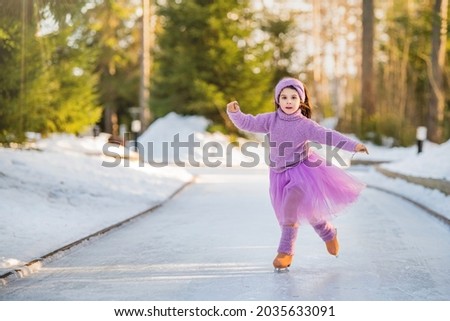 little young girl in a pink sweater and a full skirt rides on a sunny winter day on an outdoor ice rink in the park