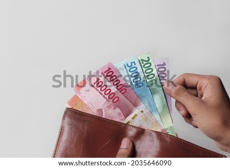 a man's hand takes and shows money from a wallet isolated on white background, rupiah is the currency of Indonesia