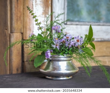 A small bouquet of wildflowers and blue New Belgian asters in a metal sugar bowl