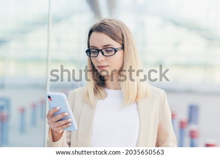 portrait of a serious business woman with glasses blonde reads the news from a mobile phone uses the application to rewrite messages