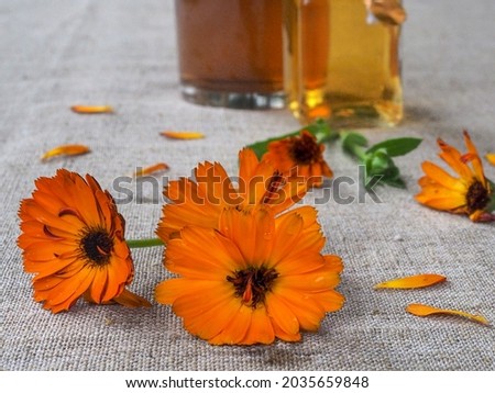 Flowers and petals of calendula officinalis on a gray linen tablecloth, in the background a decoction and infusion of calendula flowers in glass glasses