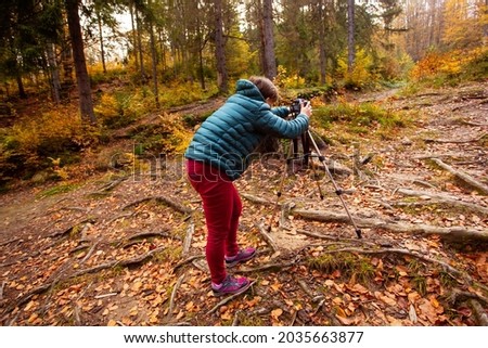 Travel photographer use camera and tripod to make photos of autumn forest. Landscape photography