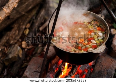 A pot of hot food in the forest, outdoor recreation at night. Hiking, travel and wilderness recreation, cooking soup over the fire. Royalty-Free Stock Photo #2035672859