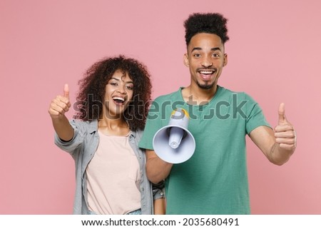 Cheerful funny young african american couple in love woman man in gray green casual clothes posing scream in megaphone showing thumbs up like isolated on pastel pink color background studio portrait